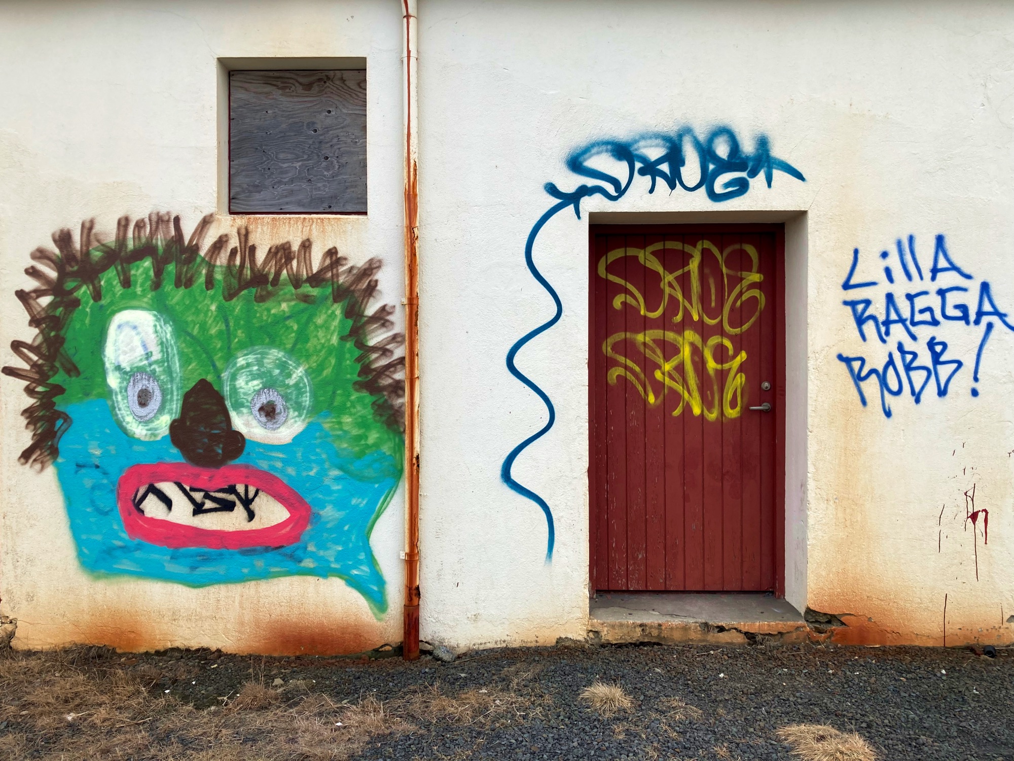 A red door covered in graffiti and a small boarded-up window.