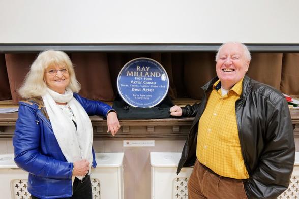 A man and a woman, relatives of Ray Milland, standing on either side of his blue commemorative plaque during an exhibition in Neath.