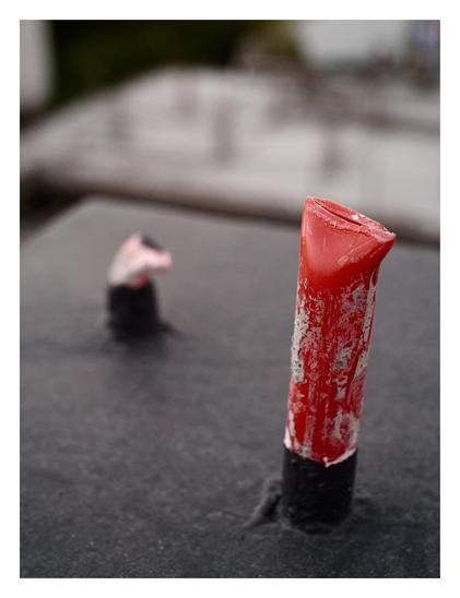 A weathered, red-painted tube protruding from a dark, textured surface. The tube is crimped shut at the top and has peeling paint revealing gray underneath. A second, similar object is blurred in the background due to a shallow depth of field. - Google Gemini 3.1 Pro Preview
