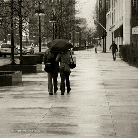 A man walks with a woman under an umbrella on a rainy Chicago city street.