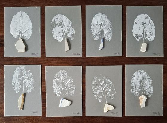 8 PostkARTenUnikate auf grausilberfarbenem Grund mit jeweils einem weißem Abdruck eine Meermangold-Blattes, das aus einem Scherbenfundstück "wächst".
Tiny Art by Teena