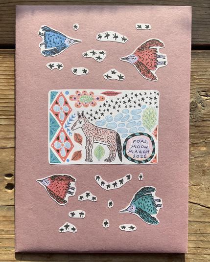 A handmade envelope with stickers on it of a foal, stars, flying birds, and patterns.