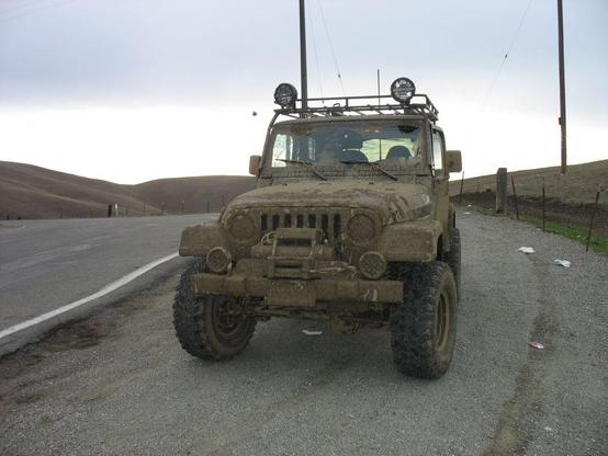 A Jeep that is well-covered with mud is parked on the side of the road.