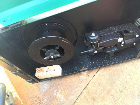 An empty black plastic reel inside a fluxcore welding machine. On the right is the feed mechanism and on the left a small handmade wooden block for storing different size nozzles inside the same compartment.