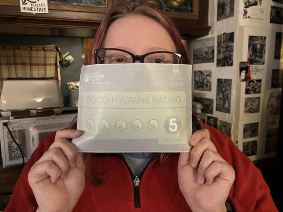 One of our volunteers holds up the window sticker that's just been awarded to us, showing a 5-star kitchen hygiene rating.
