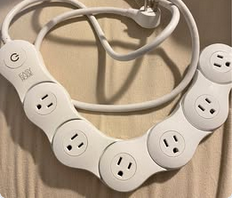 Color image of a power strip with six separate movable outlets, all of which appear to have surprised faces. Image shows the power strip in a U-shape on a table, the faces in various states of shock and surprise.