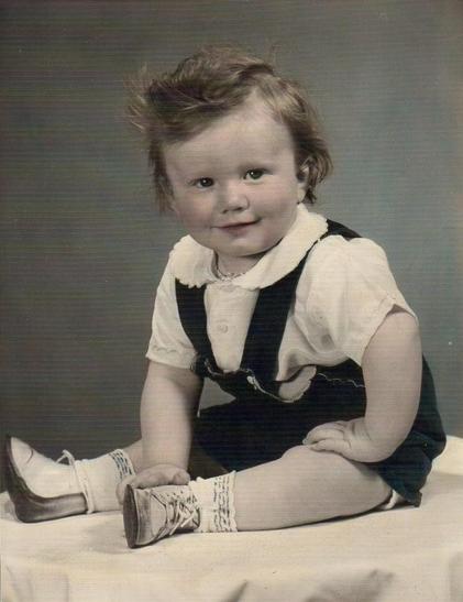 Me at 1 year old sitting for a professional photograph with curly hair and a slight smile. I was happy at that moment.
