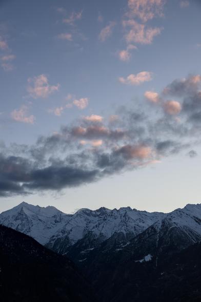 Blick auf das Weisshorn mit Brunegghorn im abendlichen blau-rosa Farbton. Am Himmel hat es kleine Wölkchen, die ebenfalls blau-grau-rosa gefärbt sind. Die Berge sind eingeschneit und verschwinden gegend den Talgrund hin im Dunklen Schwarz.