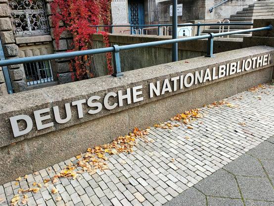 Foto der Deutschen Nationalbibliothek Leipzig, aussen. An einer Mauer steht der Schriftzug "Deutsche Nationalbibliothek".
Foto: S. Hagenhoff 2025