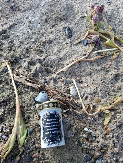 Eine elektrische Trauerkerze und welke Tulpen liegen am Strand.