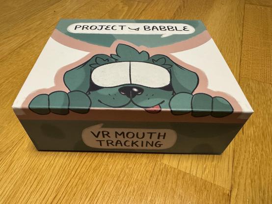 Photo of the Project Babble box, it has a greenish blue cartoon dog with a vr headset on it with their tongue sticking out the side of their mouth. The box says “mouth tracking” in a speech bubble below.