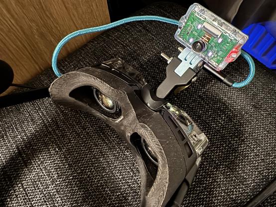 Photo of the mouth tracker mounted on the Beyond 2E headset so it can see the lower face of anyone wearing the headset. A cable leads from tracker to the headset. The headset itself is upside down not to have it resting on the tracker