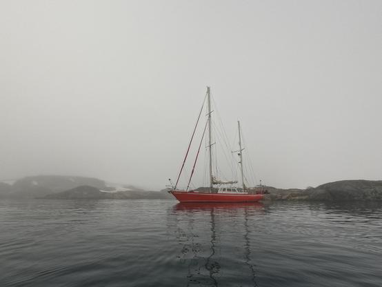 Red yacht in front of an island, cloudy weather