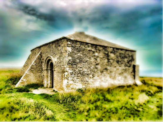 An ancient chapel in a green grassland beneath a blue sky.