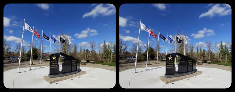 A row of flags and a black memorial in front, under a blue sky with a few clouds.