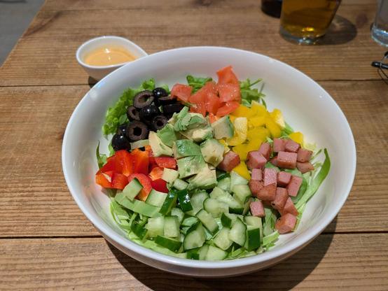 A large bowl of Cobb salad, un-mixed, with dressing in a small decanter to the side