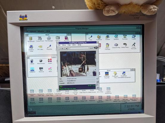 Photo of a beige CRT monitor showing a Windows 3.11 system running RealPlayer 5.0. A streaming video channel called Watch and Learn is playing, showing the vacuum cleaner episode of The Secret Life of Machines.