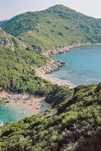 Porto Timoni is one of the most beautiful places in Corfu. It is a cape with a double beach with turquoise water and light sand. Many hills covered with greenery and trees, the sky is clear and cloudless, the sun is shining.
