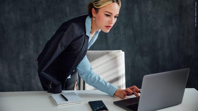 Eine Frau steht an einem Schreibtisch und schaut etwas an einem Laptop an. Ist es Chefs erlaubt, die Mails ihrer Mitarbeiter zu lesen? (Foto: IMAGO, IMAGO/YAY Images)