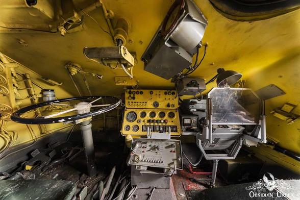 An abandoned yellow OT-64 SKOT APC driver's cabin with a large steering wheel and instrument panels.
