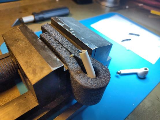A piece of foam is used to fix a airpod in the vise.
The second airpod and some tools can be seen in the periphery.