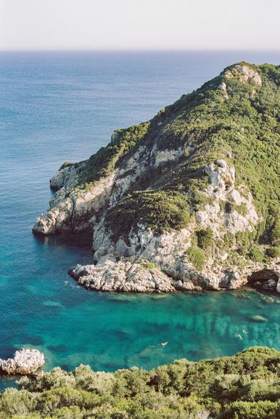 Porto Timoni is one of the most beautiful places in Corfu. It is a cape with a double beach with turquoise water and light sand. Many hills covered with greenery and trees, the sky is clear and cloudless, the sun is shining.