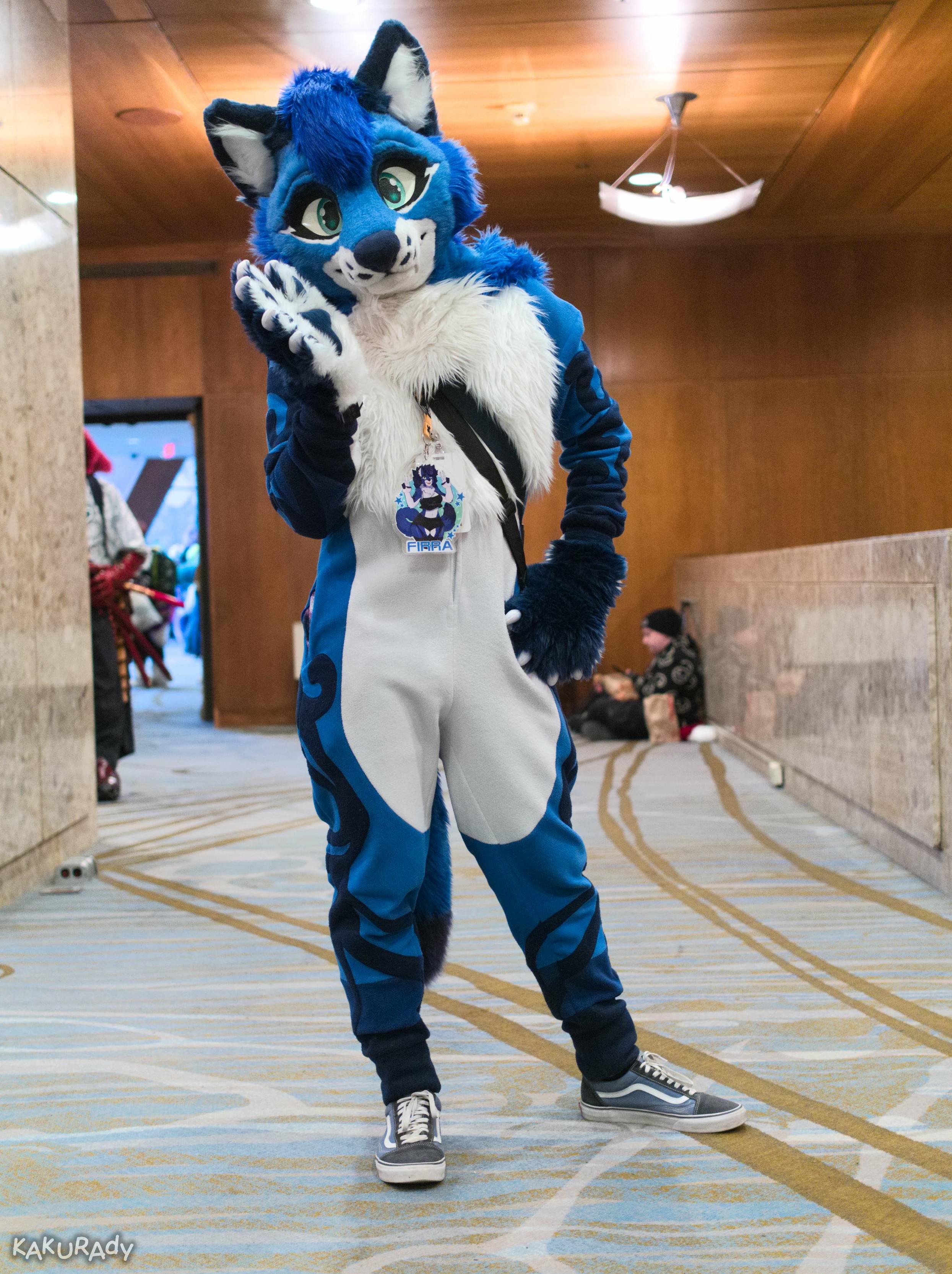 Blue wolf fursuiter wearing gray sneakers, standing in an carpeted indoor passageway, leaning on one side
