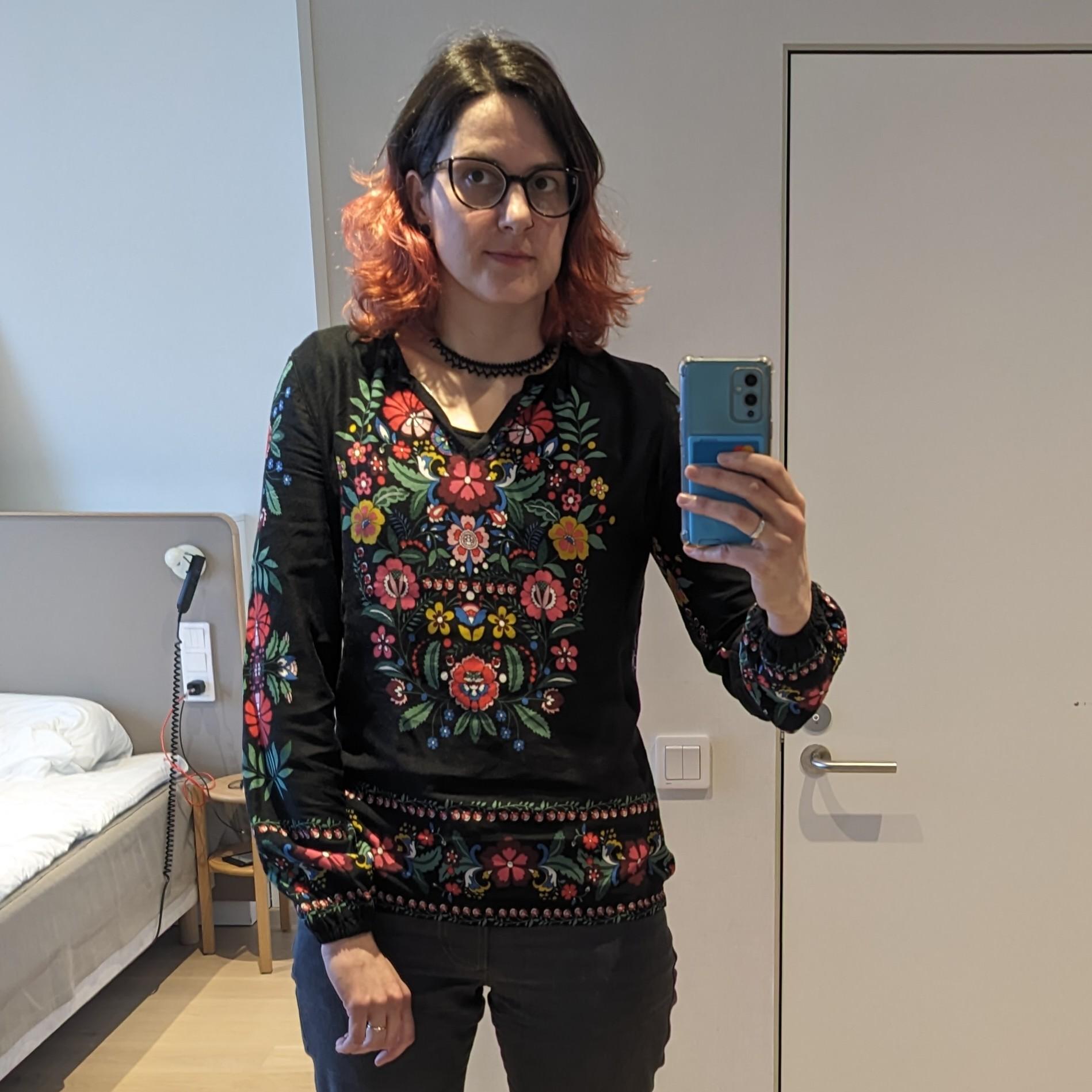 Hotel selfie of Katharina wearing a blouse with a colourful ornamental flower pattern.