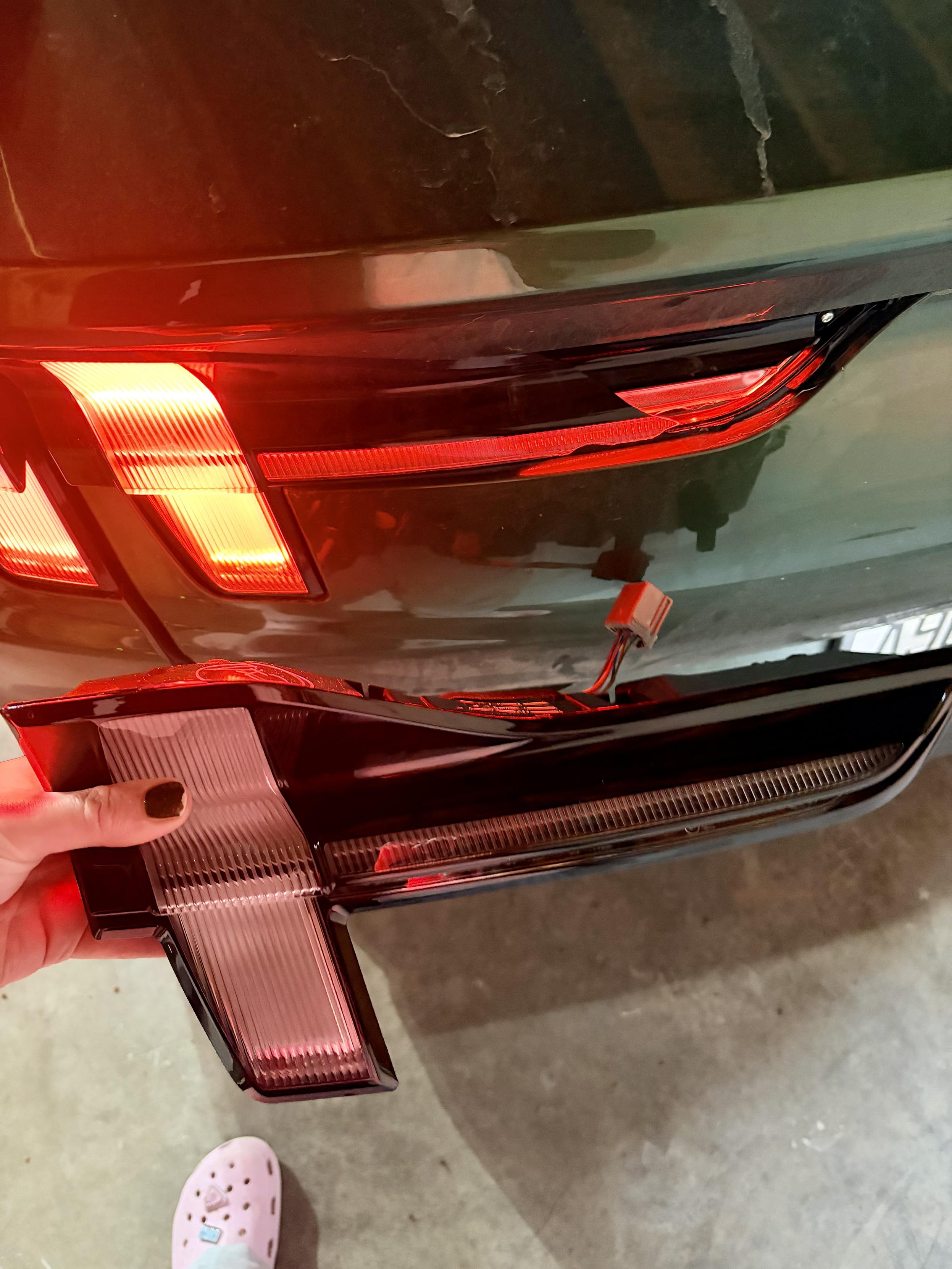Hand holding a new brake light for a ford mustang mach-e behind the parked car, showing the cracked light still on the car.