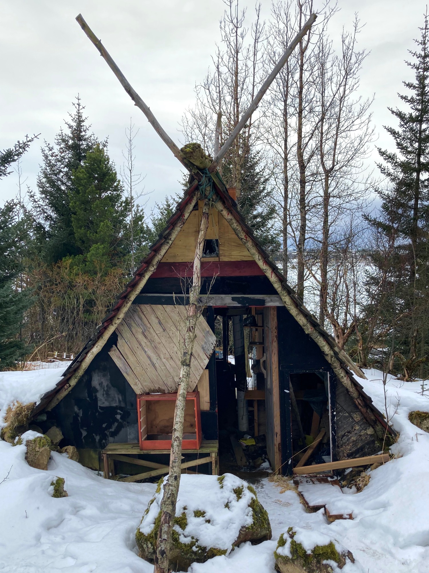 A strange looking A-frame shed surrounded by snow and trees.