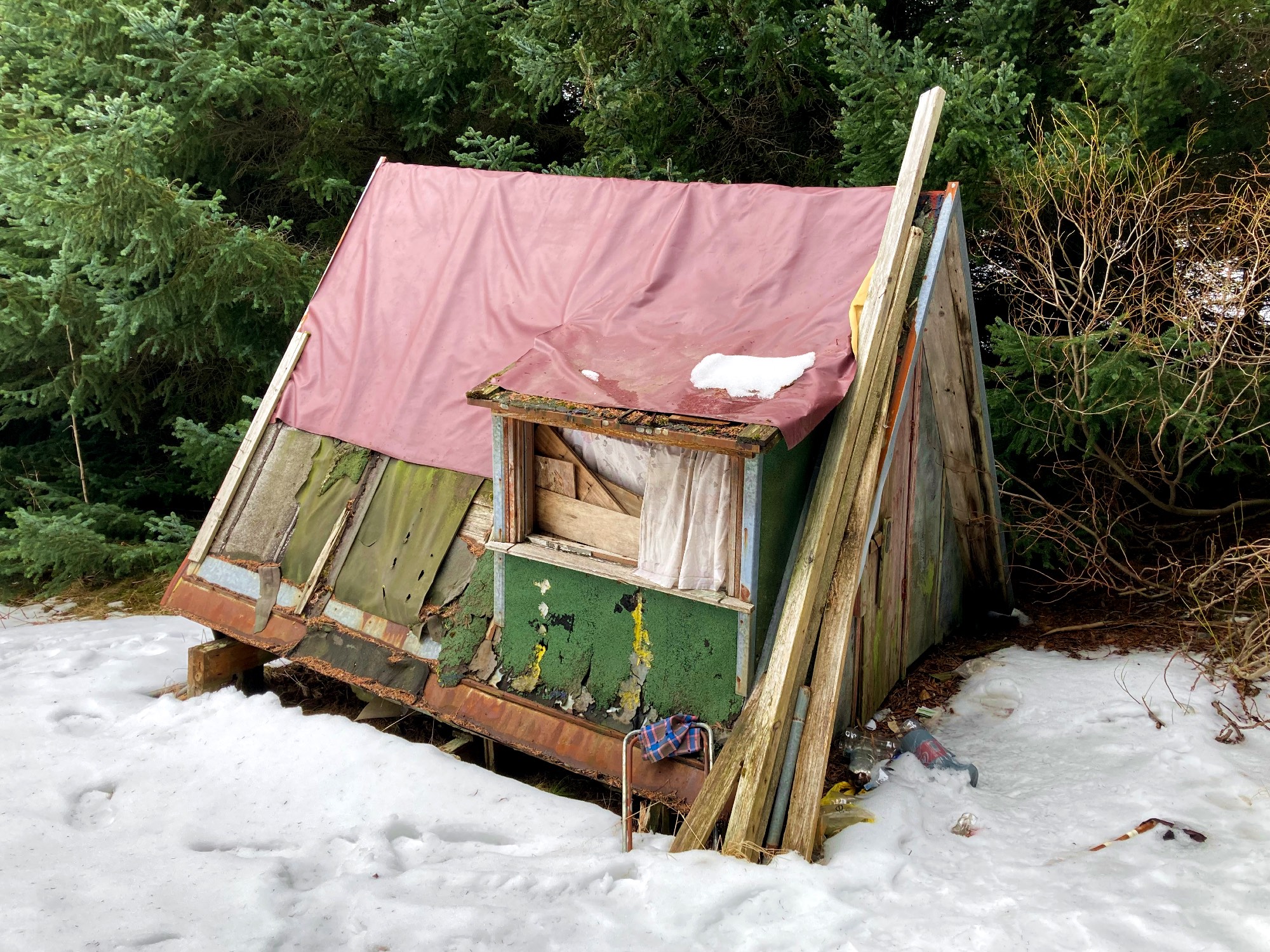 A tiny A-frame shed with a pink blanket on the roof.