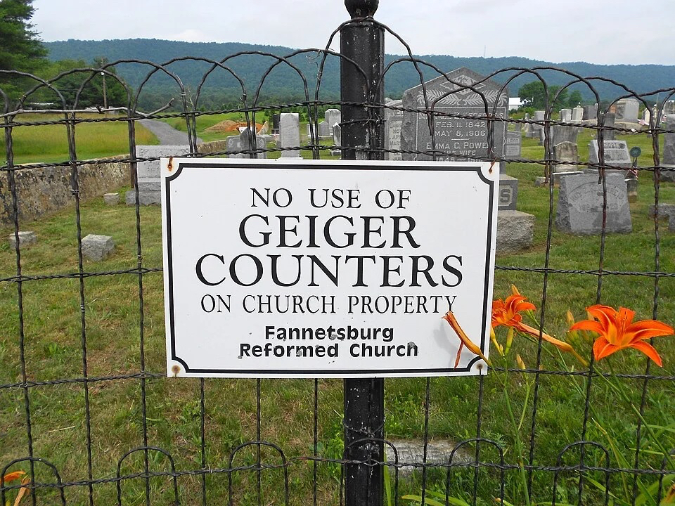 A sign on the fence of a graveyard. It reads "No use of geiger counters on church property."