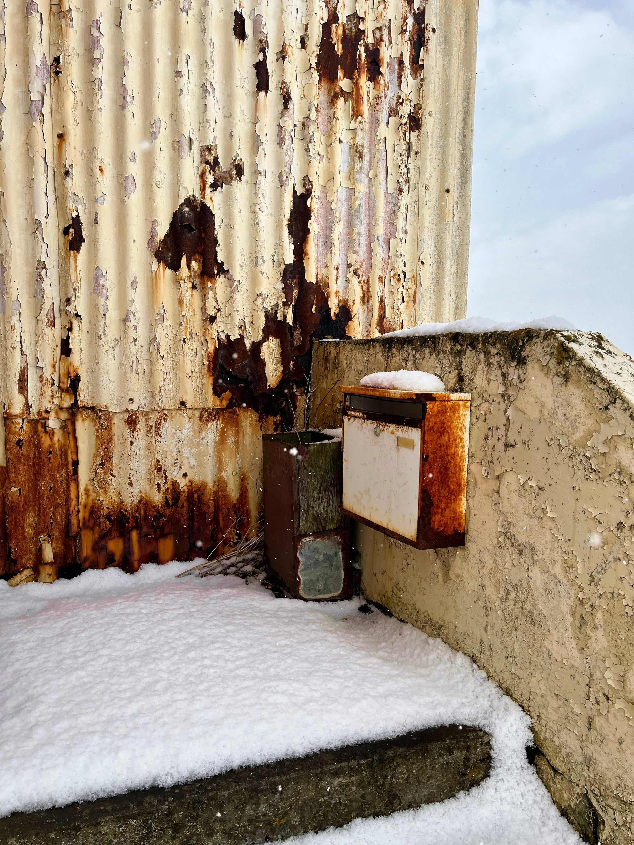 A rusty old mailbox on a rusty old house.