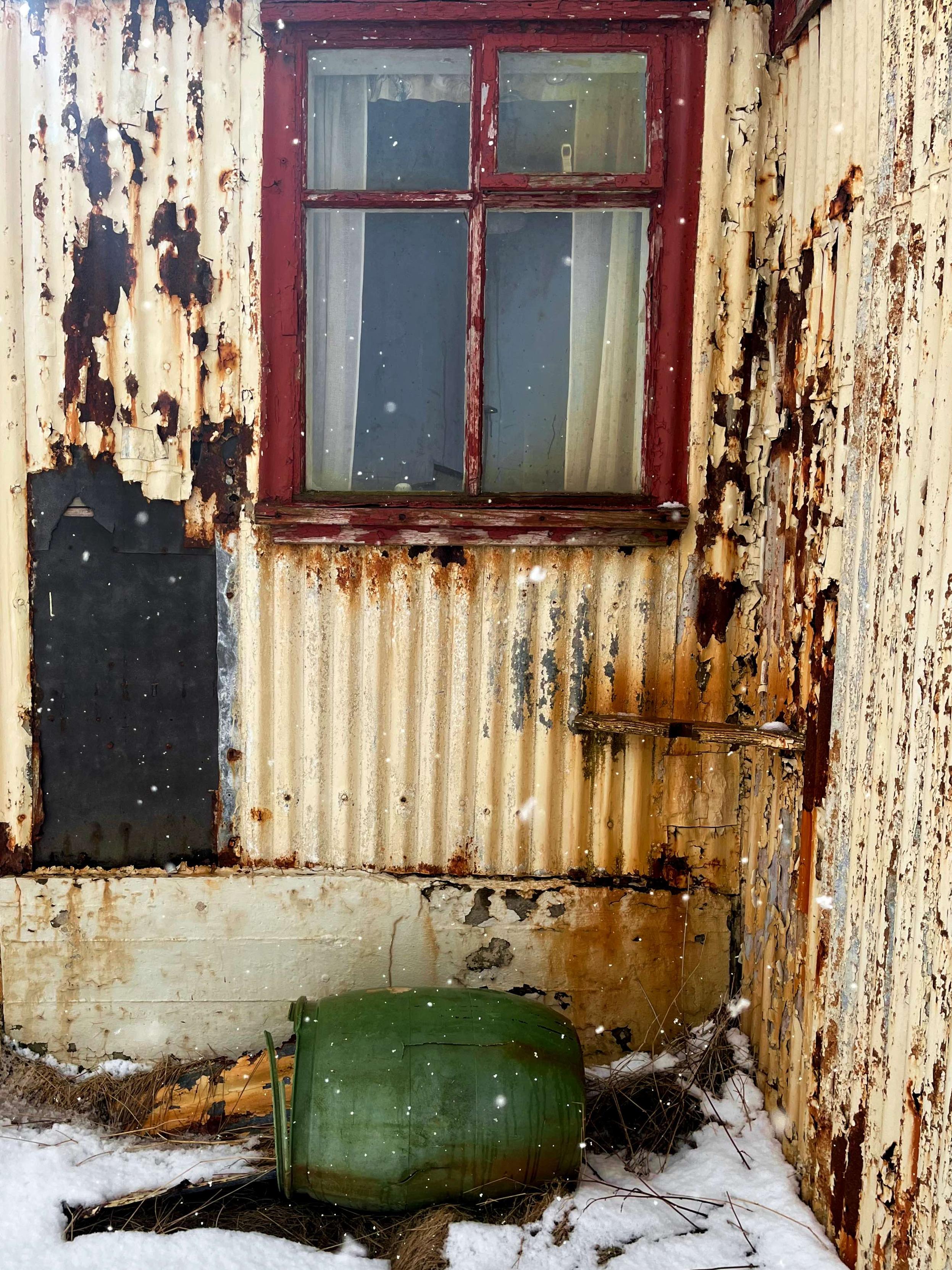 A small red window on a rusty abandoned house.