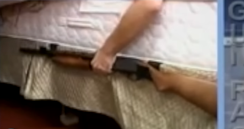 person putting a gun in a rack attached to the side of the bed