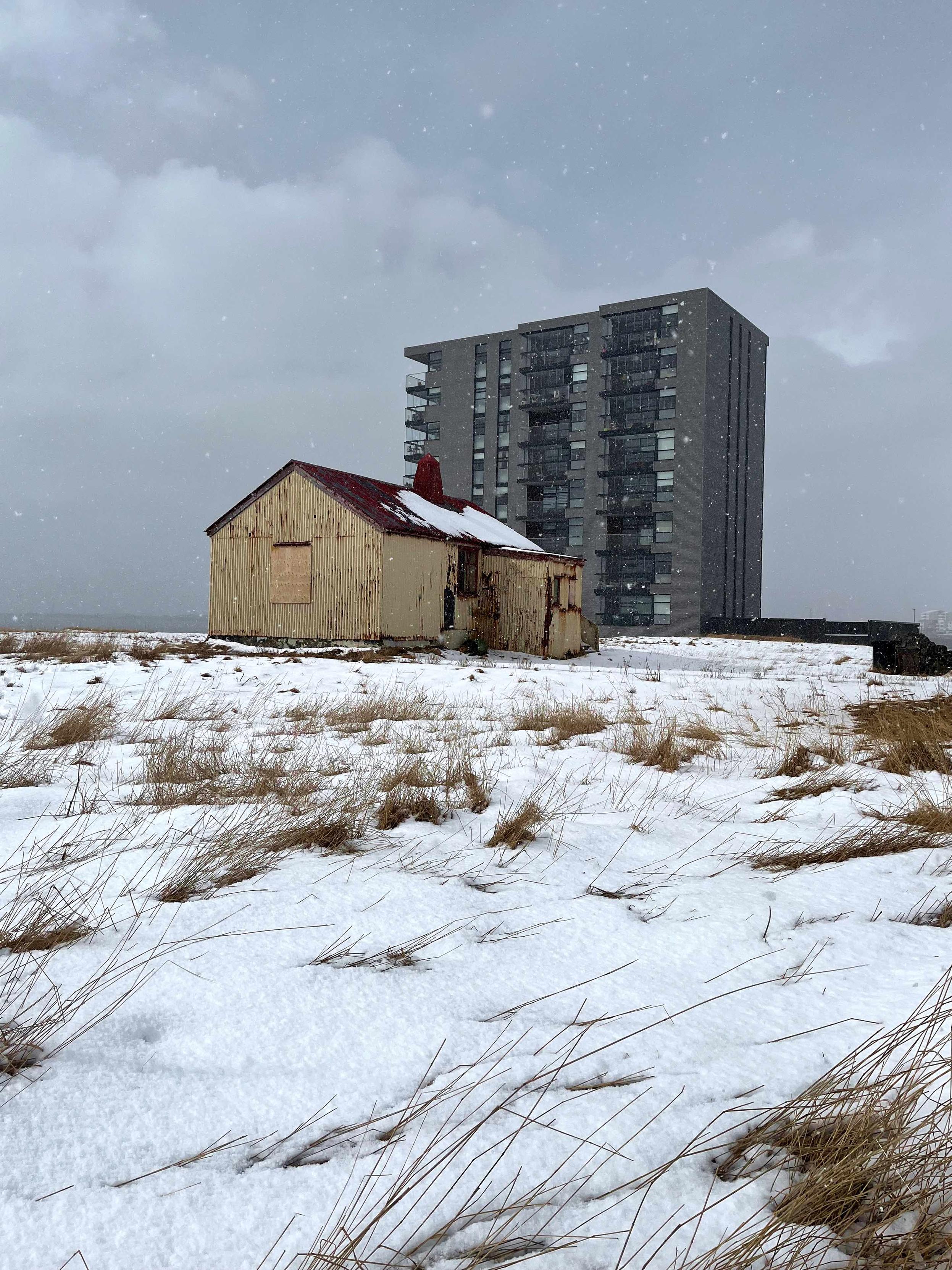 An abandoned old house with a new apartment building in the background.