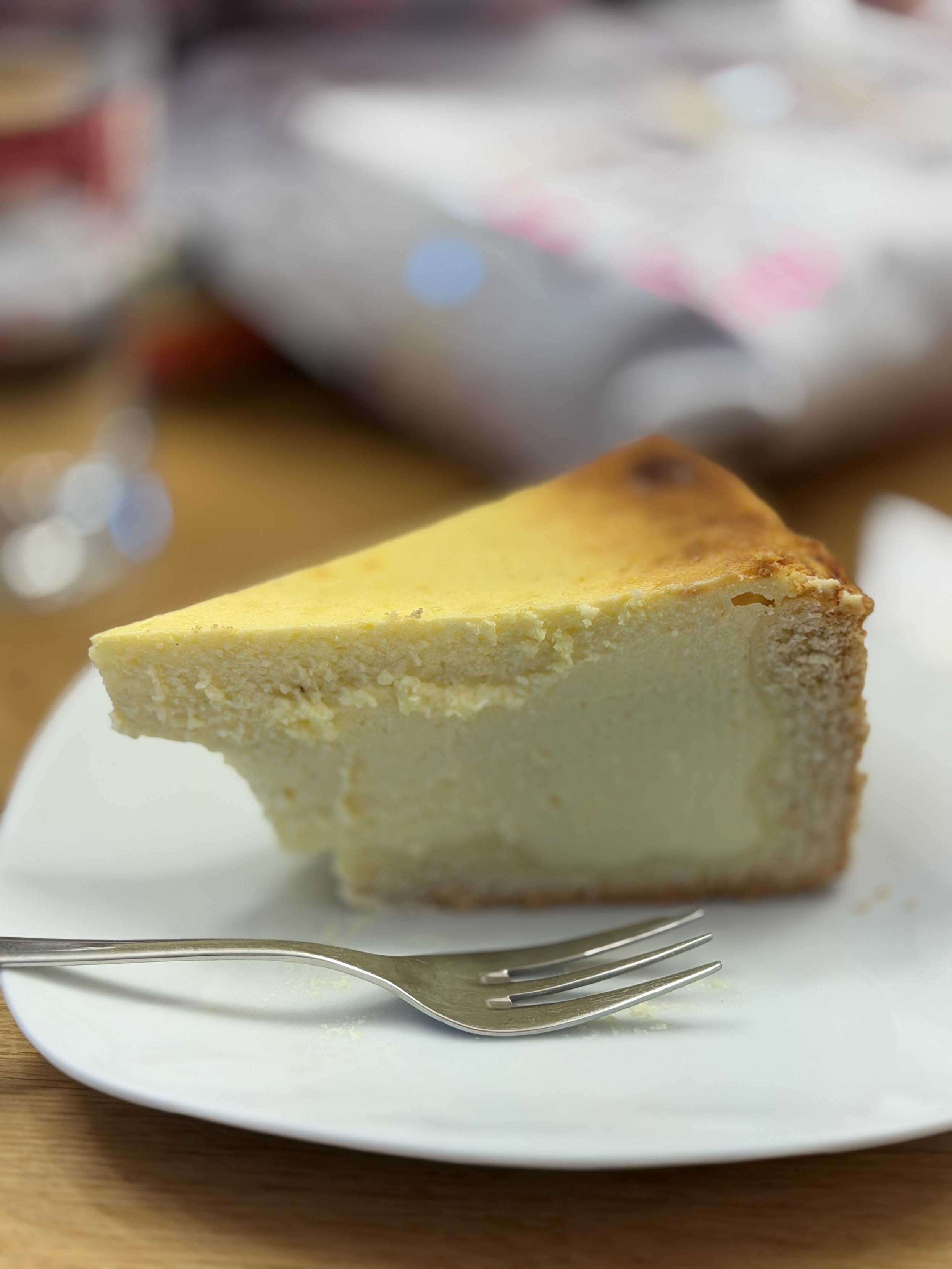 Ein Stück Käsekuchen auf einem Teller. Daneben liegt eine Kuchengabel.