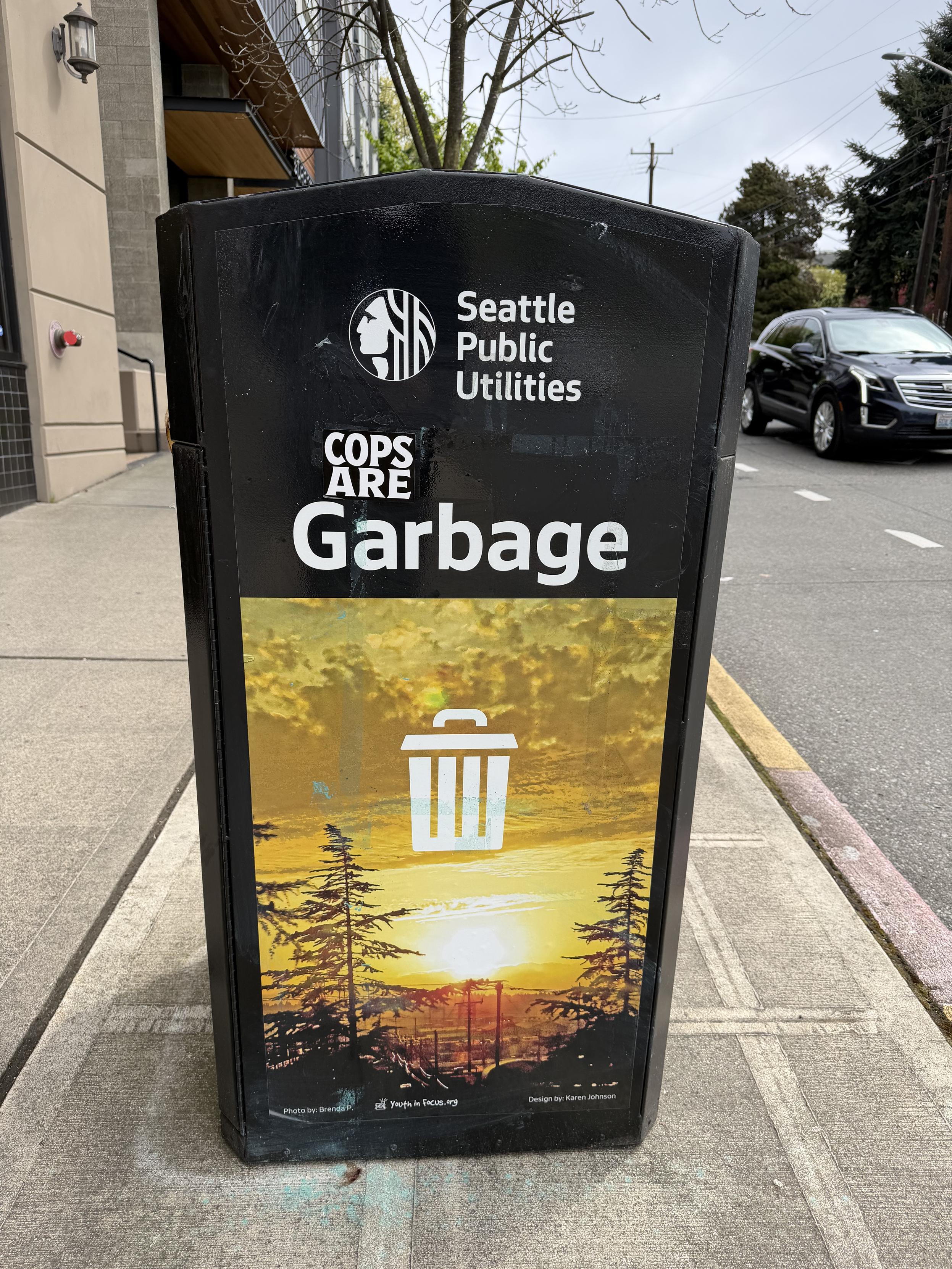 A municipal garbage can with the sticker “cops are” above the word garbage