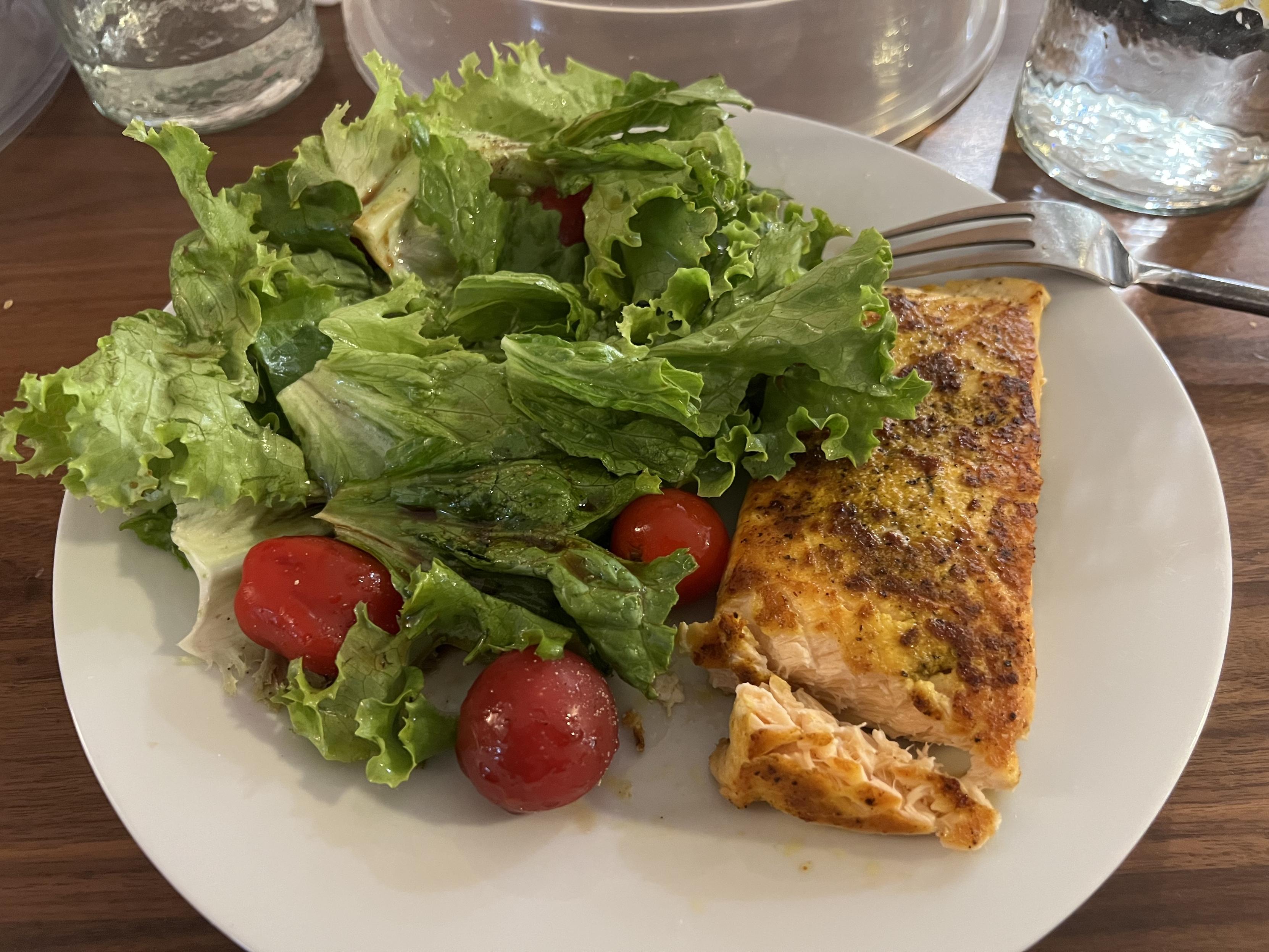 White ceramic plate with a well seasoned salmon fillet and a large side salad with lettuce and grape tomatoes and some balsamic