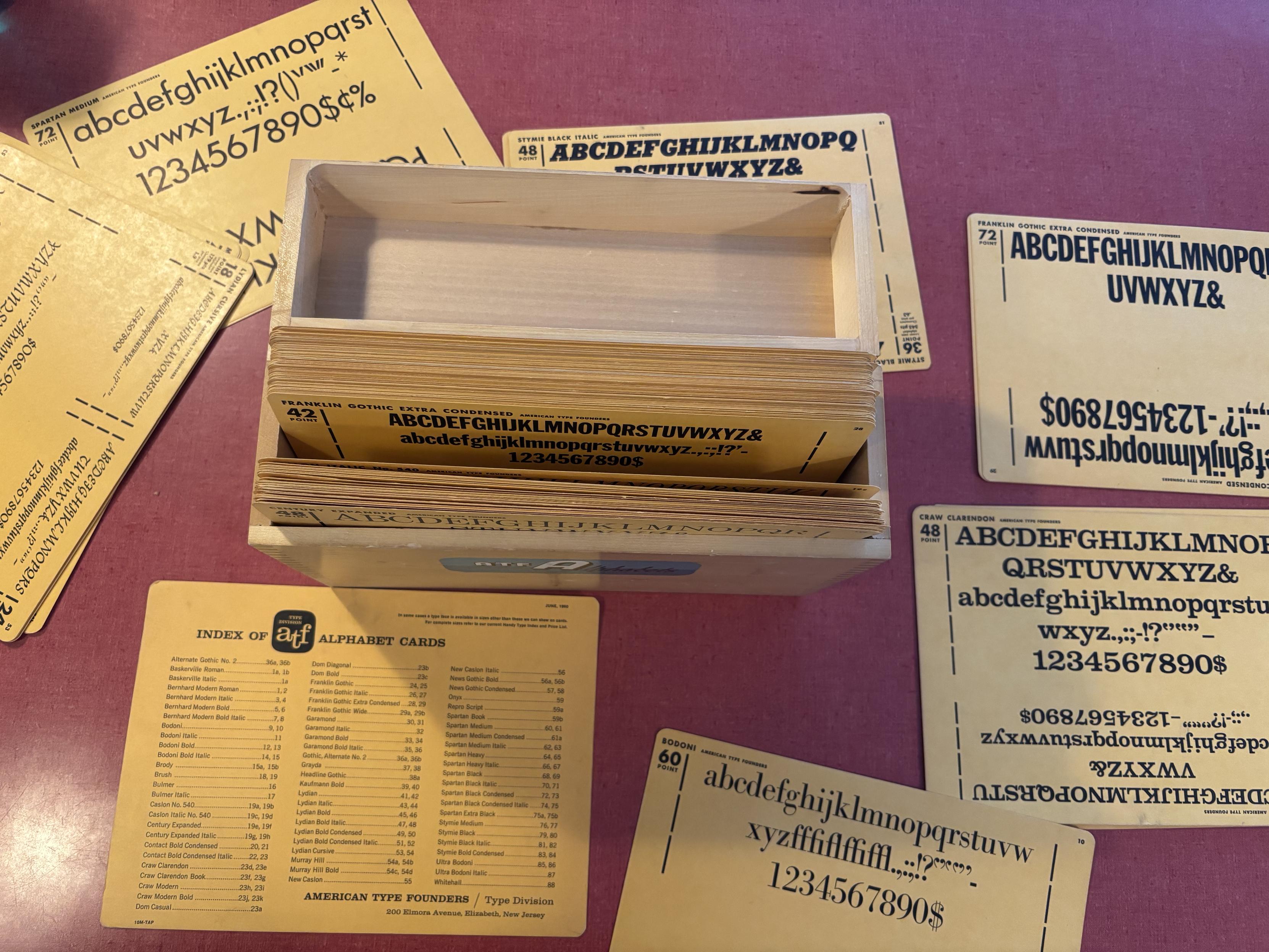 Various alphabet specimen cards on a table around an open wooden box