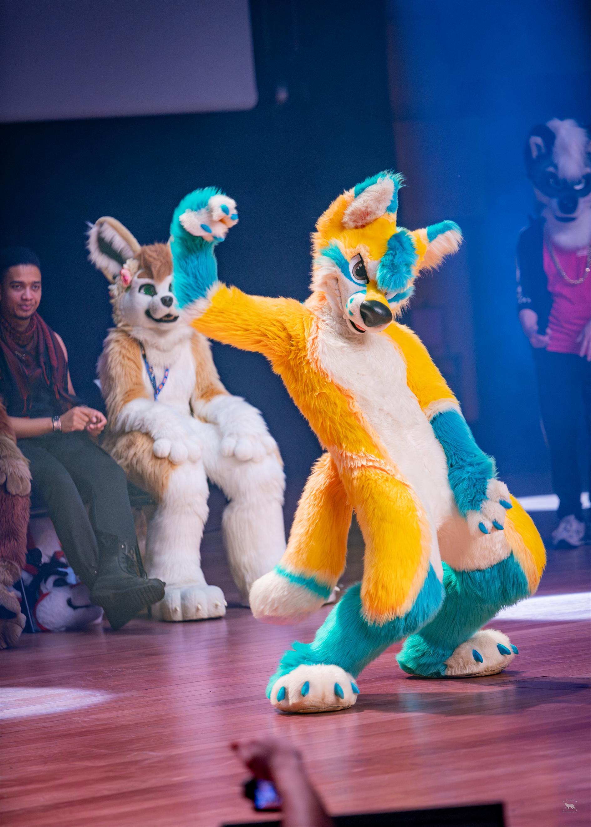yellow-cyan fursuiter performing during a dance/stage event.