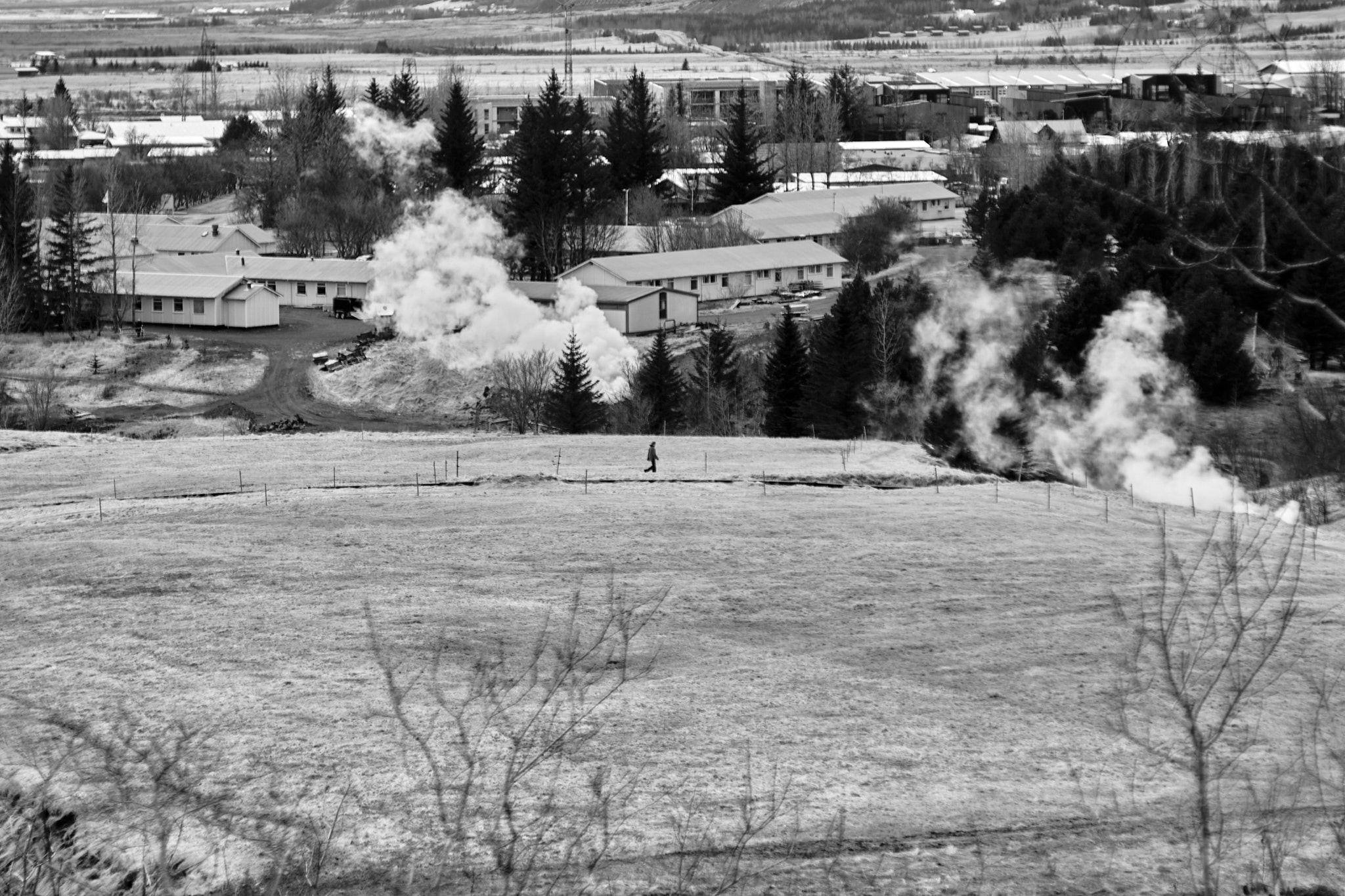A hiker cuts across a field in Hveragerði. You can see the local health resort in the background.
