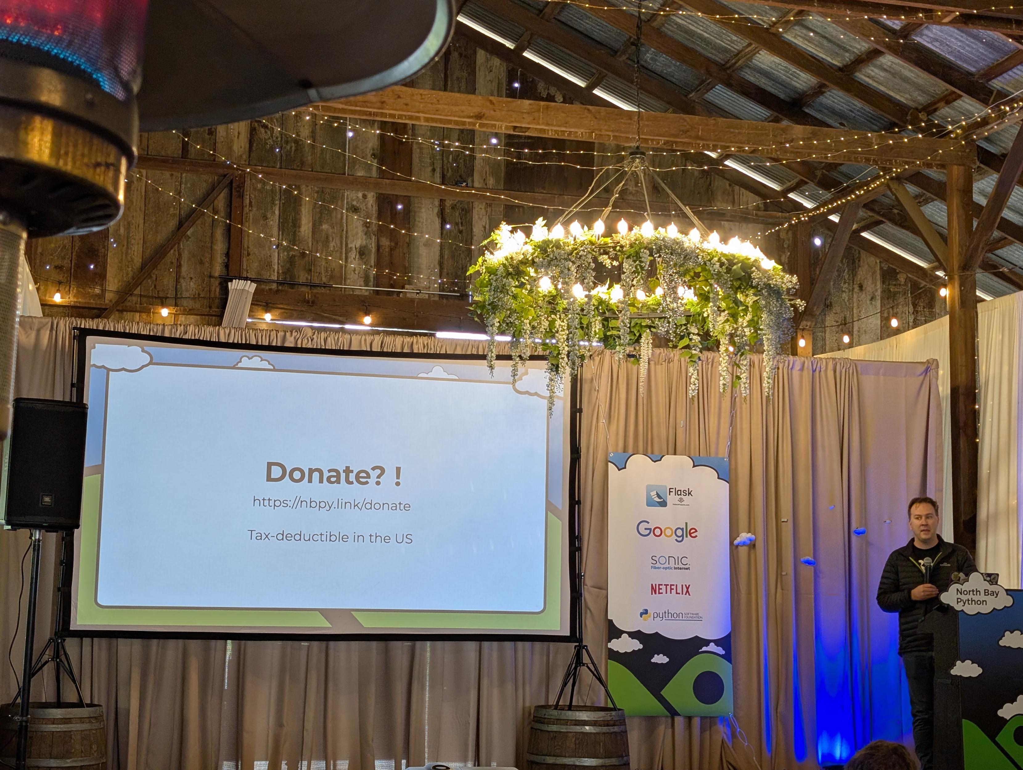 A photo of Chris on stage with a slide giving instructions for donations