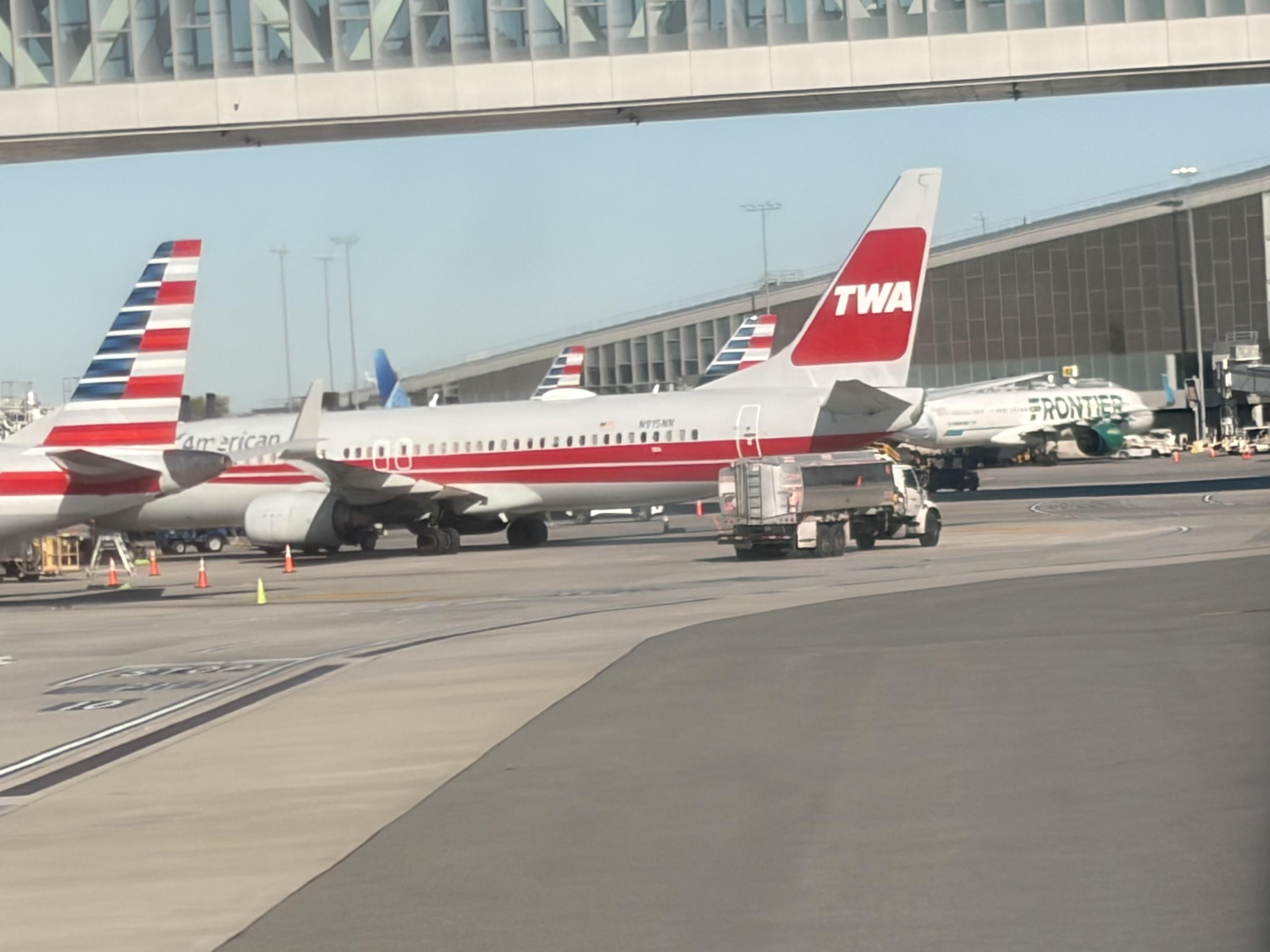 Photo of a plane parked at the gate a LaGuardia with TWA painted on the tail.