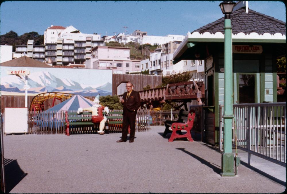 Fun Tier Town, circa 1968 A man in a suit posed near a seated clown figure on a bench. The clown looks pretty bright and colorful