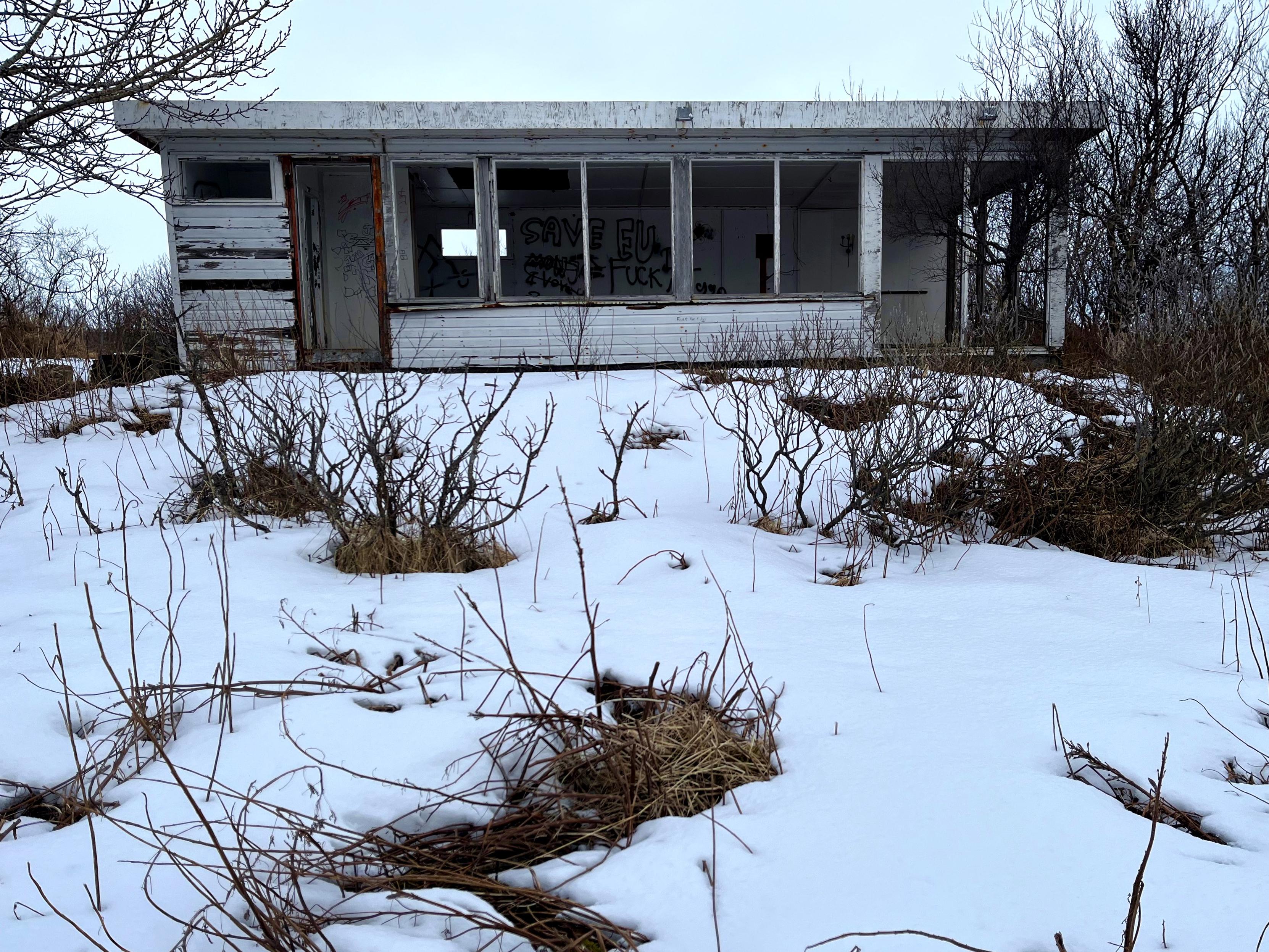 An abandoned summer cabin surrounded by snow and trees.
