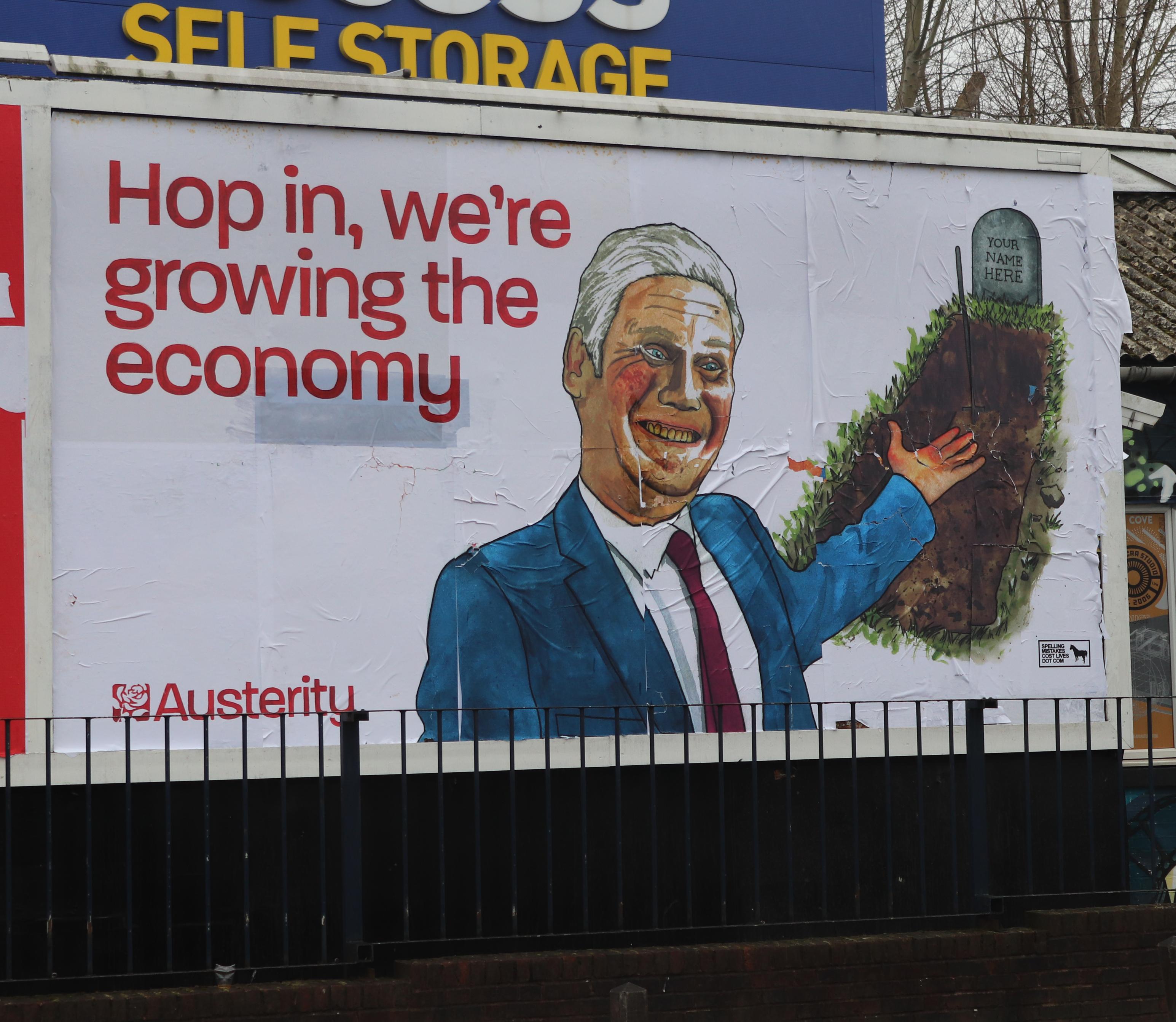 Photo of a subvertised billboard done like a labour ad, big picture of a queasy looking starmer with his arm out towards a grave with the words 'your name here' on the gravestone. Headline: HOP IN, WE'RE GROWING THE ECONOMY. At the bottom the Labour logo text has been changed to say Austerity