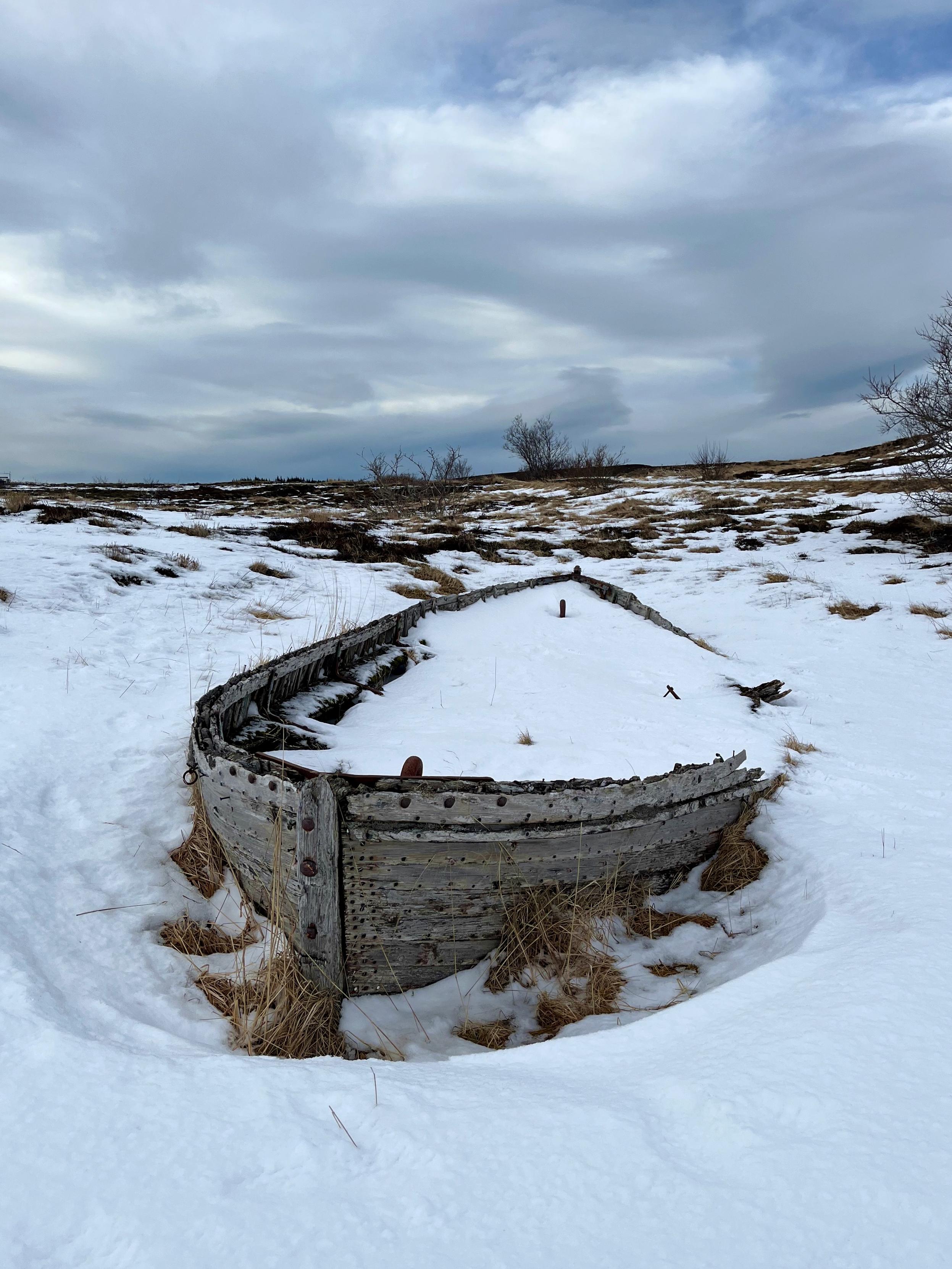An old wooden boat covered in snow, surrounded by no water whatsoever.