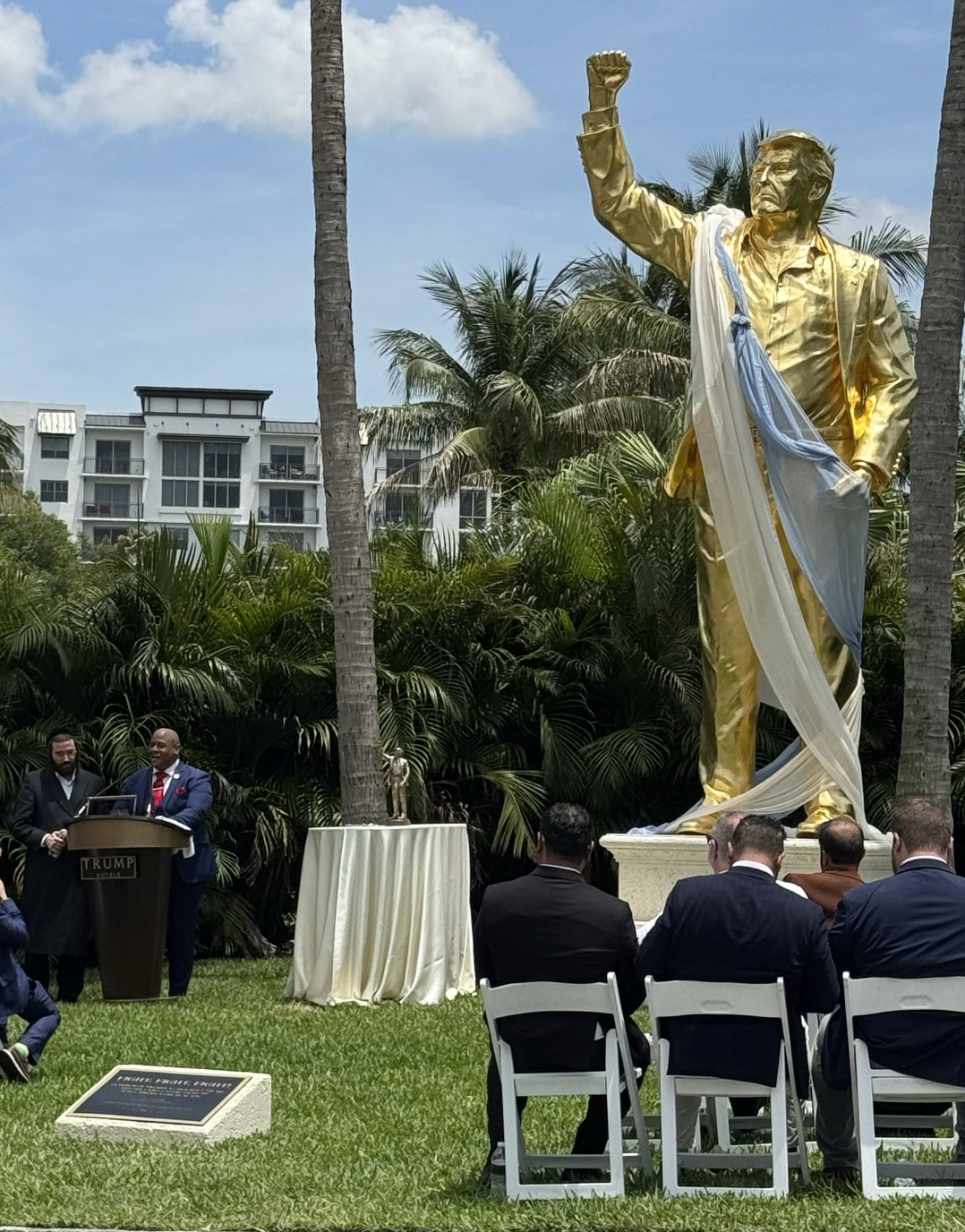 Pastor Burns speaking at the feet of a massive golden calf idol shaped like DonaldTrump
