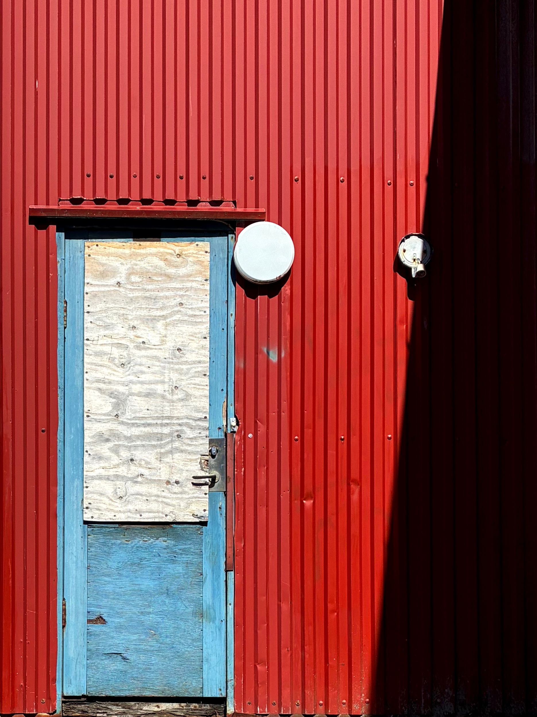 An old blue door against a red wall.
